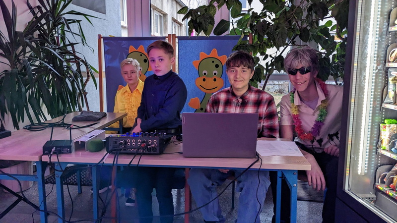 czworo uczniów w kolorowych strojach obsługujących sprzęt muzyczny